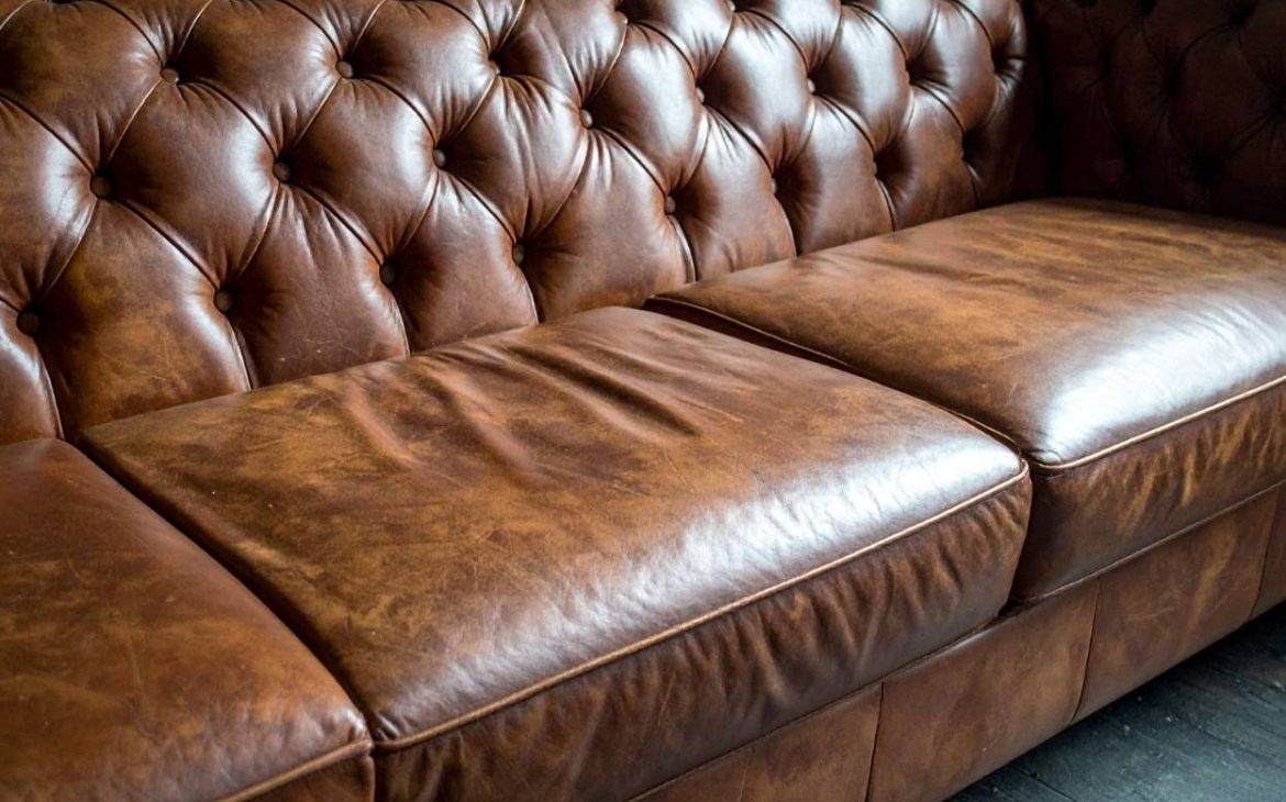Hands smoothing conditioner on tan leather armchair for restored shine.