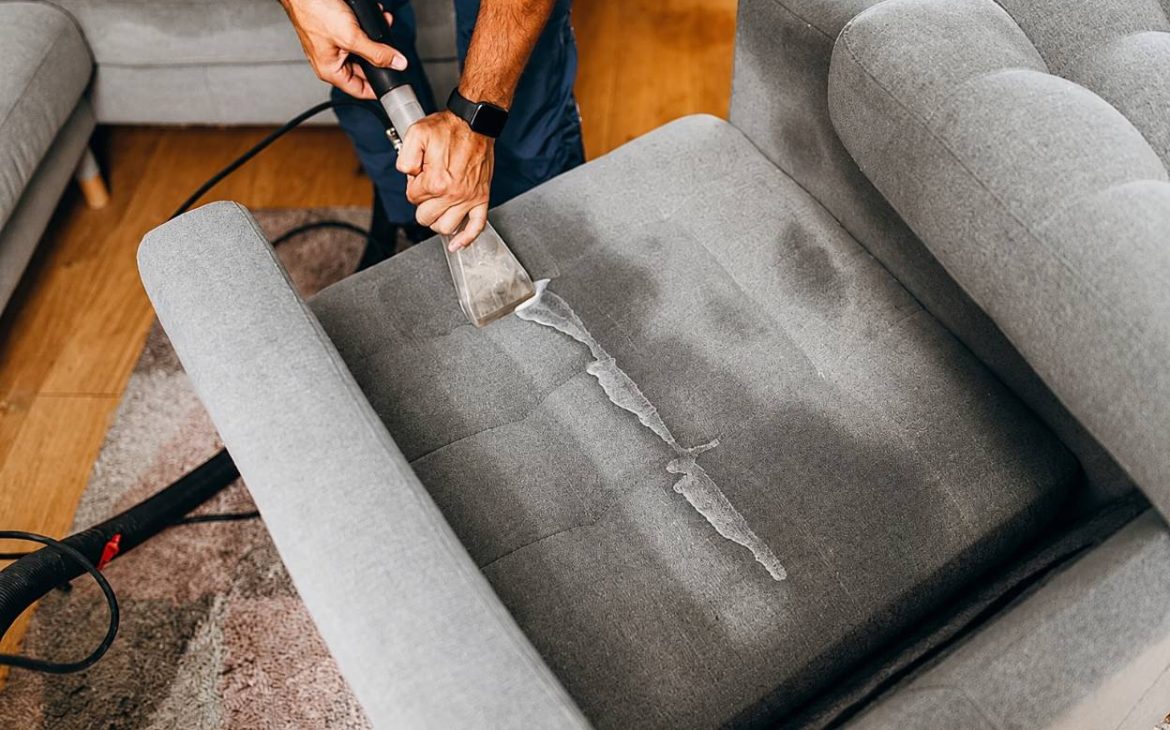 Close-up of a grey fabric sofa cushion being deep cleaned with an upholstery extraction tool during a home cleaning process.